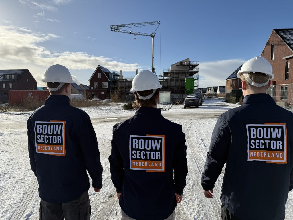 Drie medewerkers van Bouwsector Nederland in jassen met logo lopen door een straat met nieuwe huizen